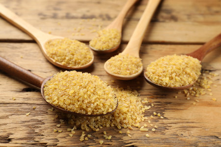 Spoons with raw bulgur on wooden table, closeupの写真素材