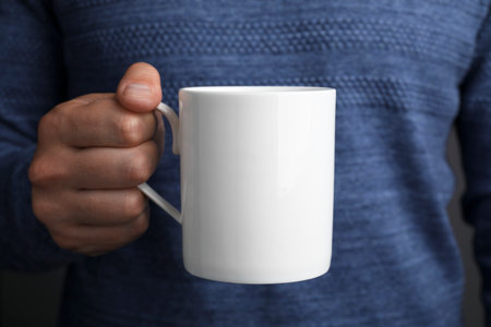 Man holding white mug, closeup. Mockup for design