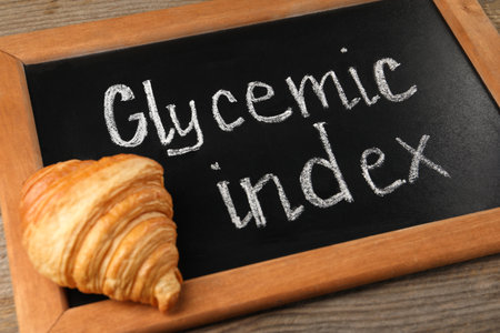 Small chalkboard with words Glycemic Index and croissant on wooden table, closeupの写真素材