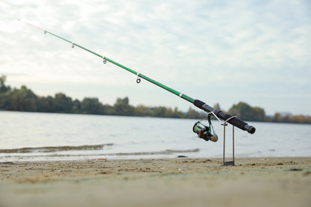 Fishing rod with reel on sand near river, space for textの写真素材