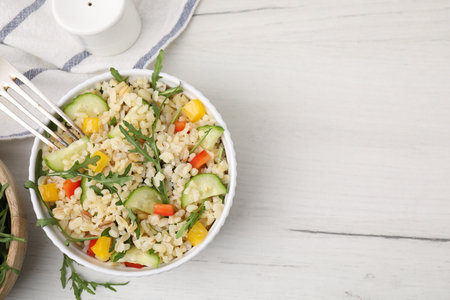 Cooked bulgur with vegetables in bowl on white wooden table, top view. Space for textの写真素材
