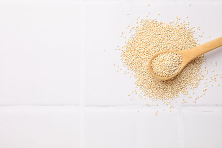 Spoon with dry quinoa seeds on white tiled table, top view. Space for textの写真素材