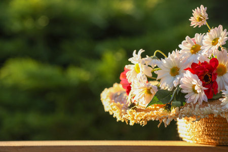 Beautiful wild flowers in wicker basket on wooden table against blurred background, space for textの写真素材