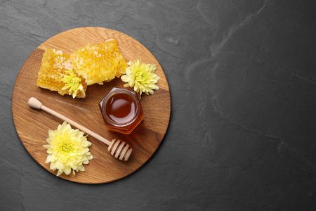 Sweet honey in jar, dipper, chrysanthemum flowers and pieces of honeycomb on gray textured table, top view. Space for textの写真素材