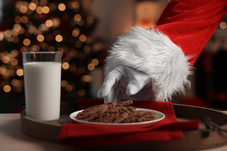 Merry Christmas. Santa Claus taking cookies from plate on table in room, closeup
