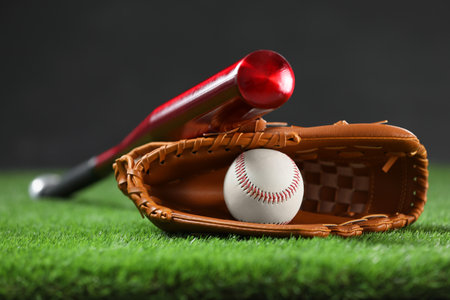 Baseball bat, leather glove and ball on green grass against dark background, closeupの写真素材