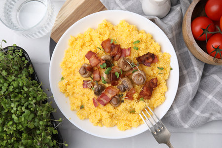 Tasty cornmeal with bacon, mushrooms and microgreens in bowl served on white tiled table, top viewの写真素材