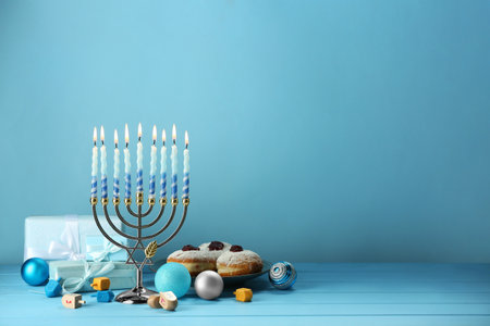 Composition with Hanukkah menorah, dreidels, donuts and gift boxes on table against light blue...
