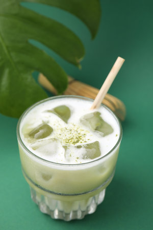 Glass of tasty iced matcha latte and leaf on green backgroundの写真素材