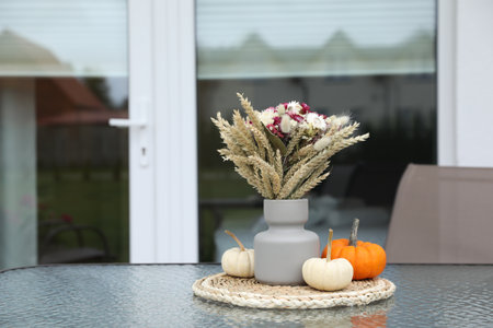 Beautiful bouquet of dry flowers and small pumpkins on glass table outdoors, space for textの写真素材