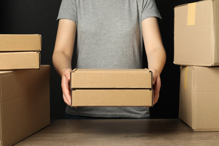 Packaging goods. Woman with cardboard boxes at wooden table, closeupの写真素材