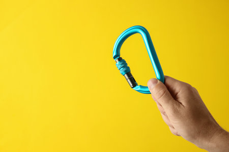 Man with metal carabiner on yellow background, closeup. Space for textの写真素材