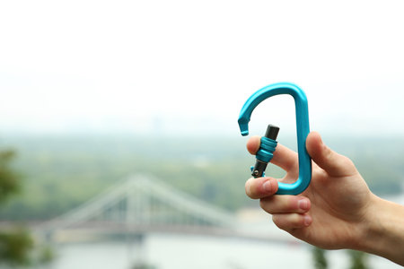 Man holding metal carabiner outdoors, closeup. Space for textの写真素材