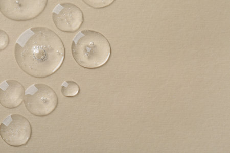 Drops of cosmetic serum on beige background, top view. Space for textの写真素材