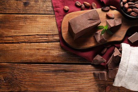 Pieces of tasty milk chocolate and cocoa beans on wooden table, flat lay. Space for textの写真素材
