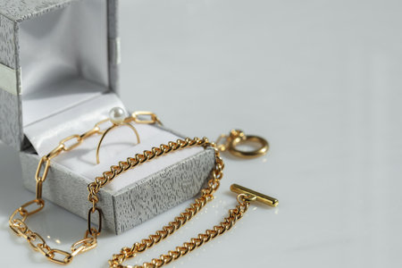 Metal chain and jewelry box with ring on white table, closeup. Space for textの写真素材