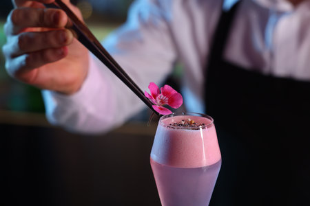 Bartender decorating fresh alcoholic cocktail with flower on blurred background, closeupの写真素材