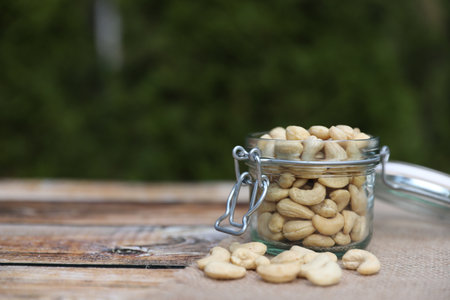 Tasty cashew nuts in glass jar on wooden table outdoors, space for textの写真素材