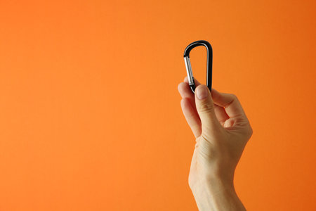 Woman with metal carabiner on orange background, closeup. Space for textの写真素材