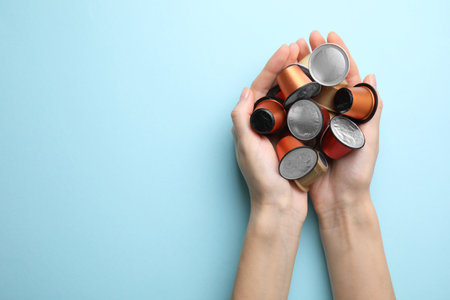 Woman holding heap of coffee capsules on light blue background, top view. Space for textの写真素材