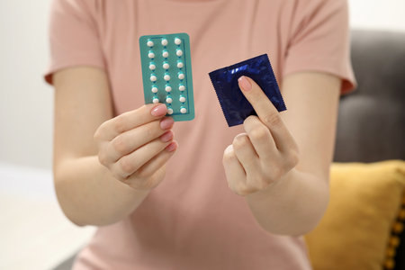 Woman holding condom and contraceptive pills on blurred background, closeup. Choosing birth control methodの写真素材