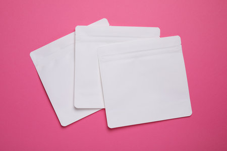 Three white bags on pink background, top view. Space for text