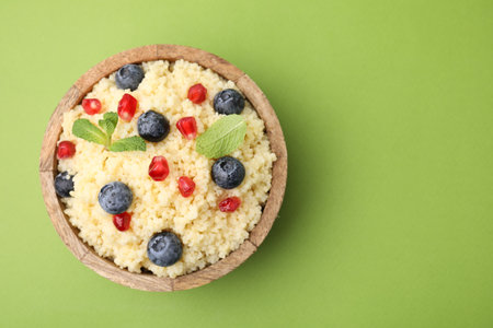 Bowl of tasty couscous with blueberries, pomegranate and mint on green background, top view. Space for textの写真素材