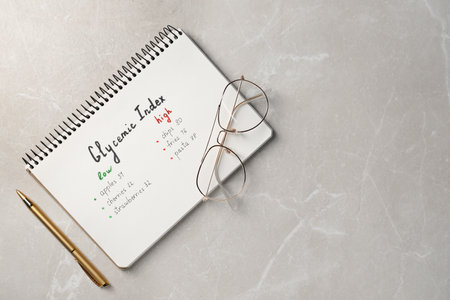 List with products of low and high glycemic index in notebook, pen and glasses on light gray marble table, top view. Space for textの写真素材