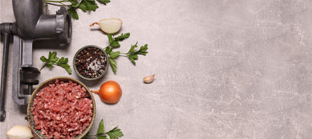 Manual meat grinder, beef mince, peppercorns, onion and parsley on light gray table, flat lay. Banner design with space for textの写真素材