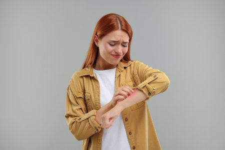 Suffering from allergy. Young woman scratching her arm on gray backgroundの写真素材