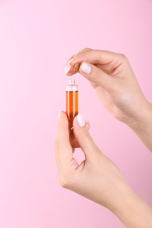 Woman holding bottle of essential oil on pink background, closeupの写真素材