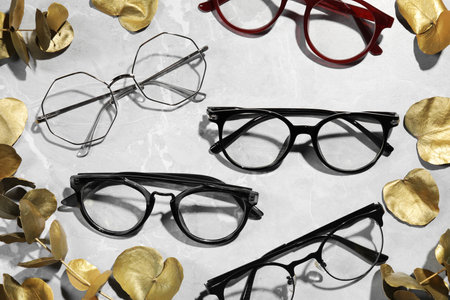 Many glasses in stylish frames and leaves on gray marble table, flat lay