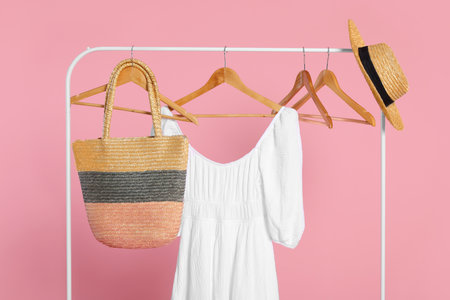 Rack with accessories and stylish white dress on wooden hangers against pink backgroundの写真素材