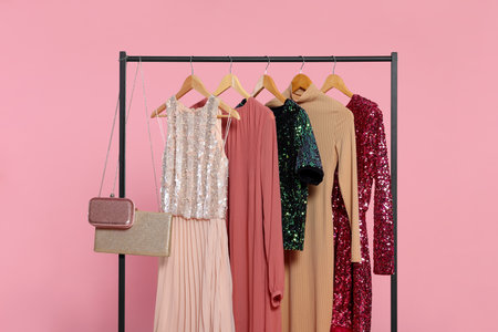 Rack with stylish women's clothes on wooden hangers and accessories against pink backgroundの写真素材