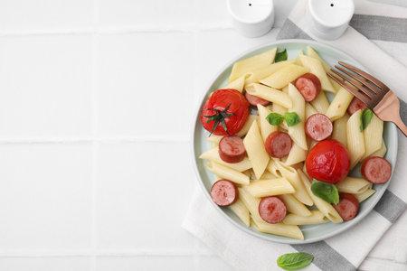 Tasty pasta with smoked sausage, tomatoes and basil served on white tiled table, flat lay. Space for textの写真素材