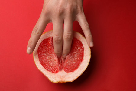 Woman touching half of grapefruit on red background, top view. Sex conceptの写真素材