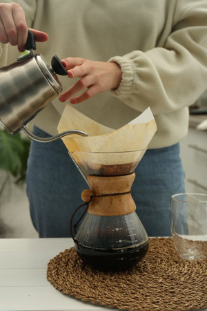 Woman pouring hot water into glass chemex coffeemaker with paper filter and coffee at table, closeupの写真素材