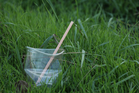Used plastic cup with straw on grass outdoors, space for text. Environmental pollution conceptの写真素材