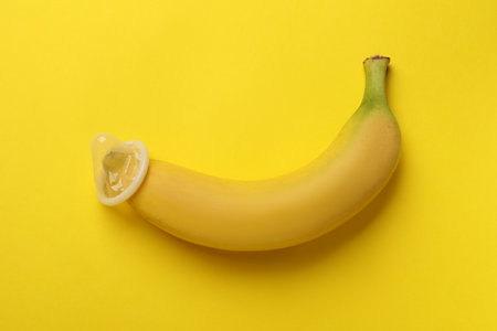 Banana with condom on yellow background, top view. Safe sex conceptの写真素材