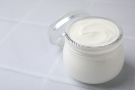 Delicious natural yogurt in glass jar on white tiled table, closeup. Space for textの写真素材