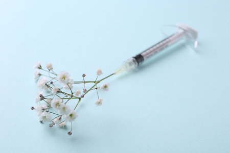 Cosmetology. Medical syringe and gypsophila on light blue background, closeupの写真素材