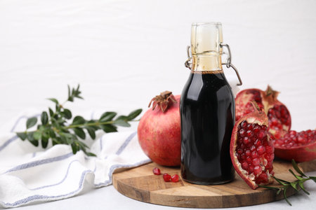Tasty pomegranate sauce in bottle, branches and fruits on light table, closeup. Space for textの写真素材