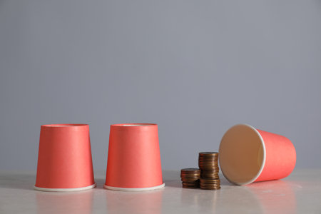 Shell game. Three red cups and coins on light table