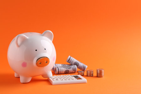 Financial savings. Piggy bank, dollar banknotes, coins and calculator on orange backgroundの写真素材