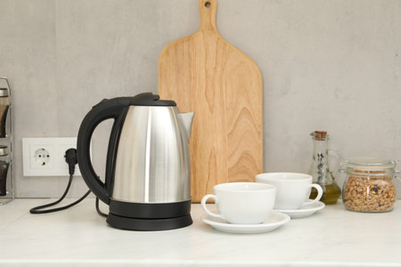 Electric kettle and cups on counter in kitchenの写真素材