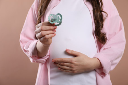 Pregnant woman holding pacifier on beige background, closeupの写真素材