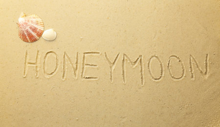 Word Honeymoon written on sand and seashells, top viewの写真素材