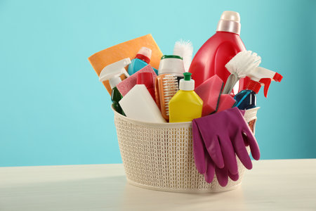Different cleaning products in basket on wooden table against light blue background, space for textの写真素材