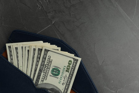 Money exchange. Wallet with dollar banknotes on dark gray textured background, top view. Space for textの写真素材