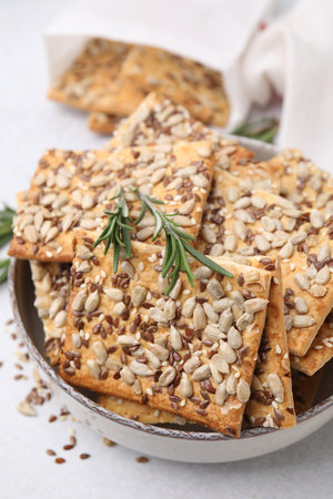 Cereal crackers with flax, sunflower, sesame seeds and rosemary in bowl on light table, closeupの写真素材